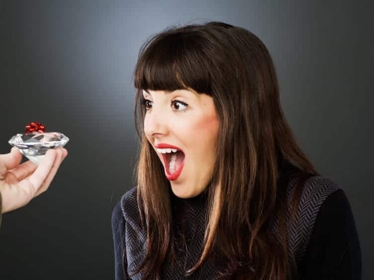 A woman expressing surprise and joy as she is presented with a diamond ring.