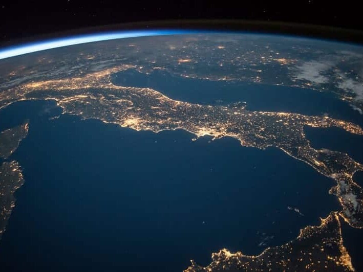 A nocturnal view from space showcasing the illuminated contours of a part of earth's landscape, with city lights tracing the outlines of coastlines and hinting at the bustling civilization below the serene celestial backdrop.