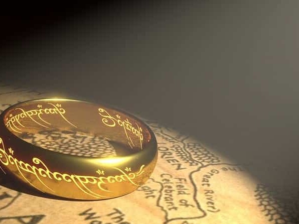 A golden ring engraved with mystical script lying on a map illuminated by a beam of light.