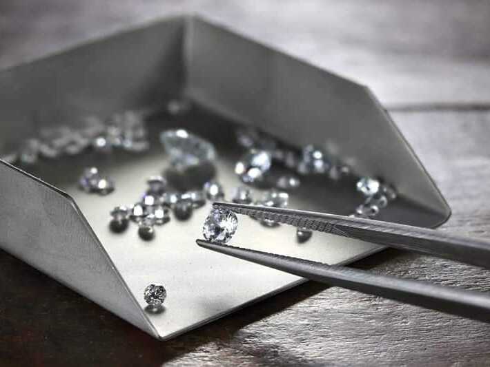 A collection of shimmering diamonds on a sorting tray with tweezers, ready for a jeweler's careful selection.