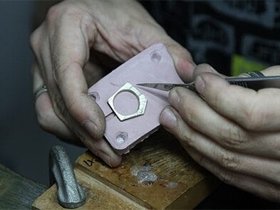 A jeweler's hands carefully crafting a ring, using a tool to shape and refine the details on a workbench.
