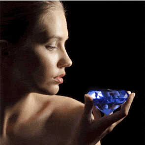 A woman gazing thoughtfully at a large, luminous blue gemstone cradled in her hand against a dark background.