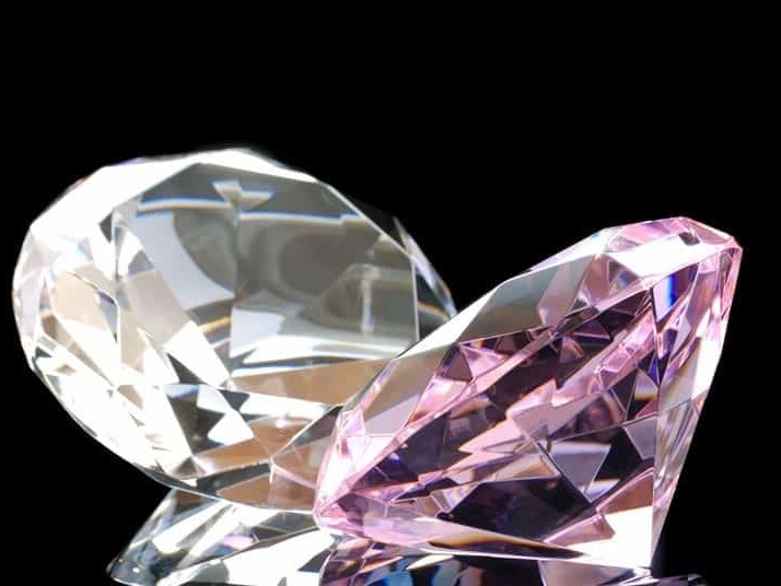 Two large, multifaceted gemstones glistening against a stark black background, one clear and the other with a pink hue.