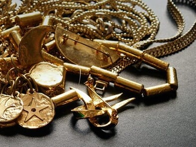 A collection of various gold jewelry pieces, including chains and charms, strewn atop a dark surface.