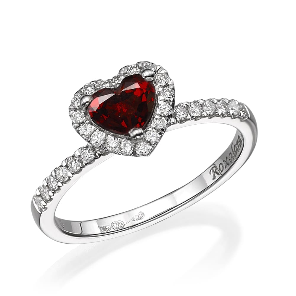טבעת יהלומים אלגנטית הכוללת אבן חן אדומה בצורת לב מוקפת בהילה של יהלומים קטנים יותר משובצים בלהקת כסף או זהב לבן מעוטרת ביהלומים נוספים.
