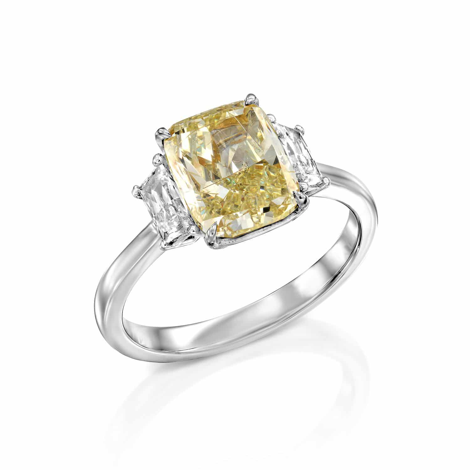 טבעת כסף אלגנטית הכוללת יהלום צהוב בחיתוך קורן ולצידו שני יהלומים לבנים טרפז על רצועה מלוטשת.