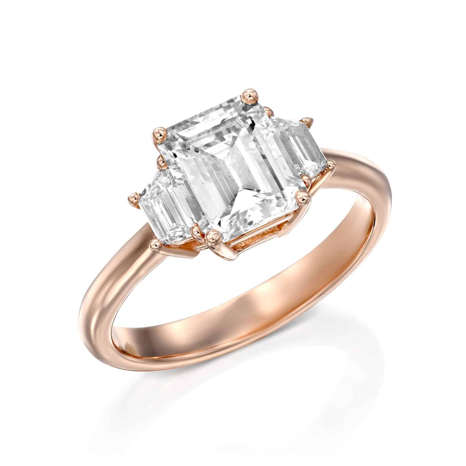 טבעת זהב ורדרד אלגנטית הכוללת יהלום בולט בחיתוך אמרלד ולצידו שני יהלומים קטנים יותר, משובצים אנכית.