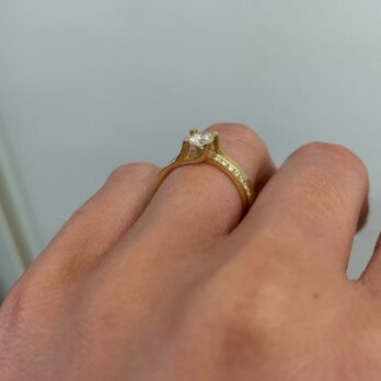 תקריב של יד עונדת את טבעת אירוסין דגם ימית, רצועת זהב עם יהלום סוליטר, המציגה את עיצוב הטבעת והתאמה על האצבע ב-38% הנחה.